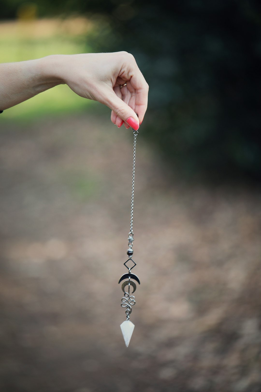 A hand holding a dowsing pendulum on a chain